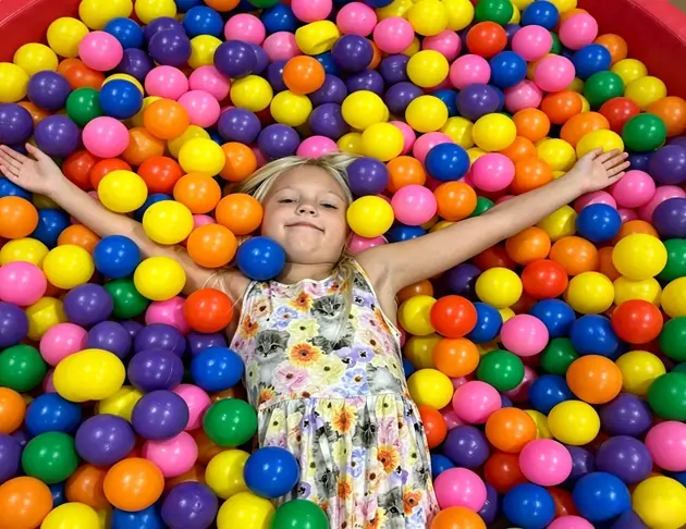 Little girl relaxing in colorful plastic ball pit indoor playground